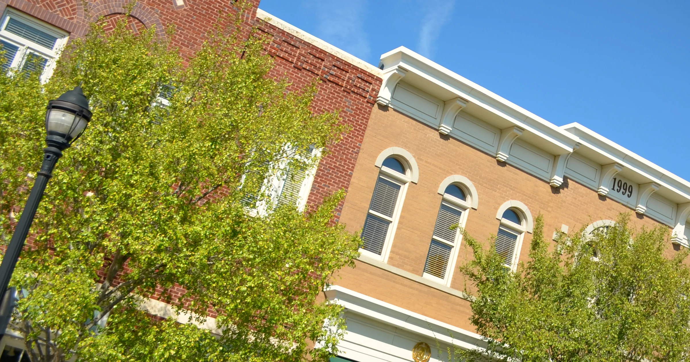 Brick and cream storefronts with arched windows and leafy trees at Southlake Town Square, Southlake, Texas